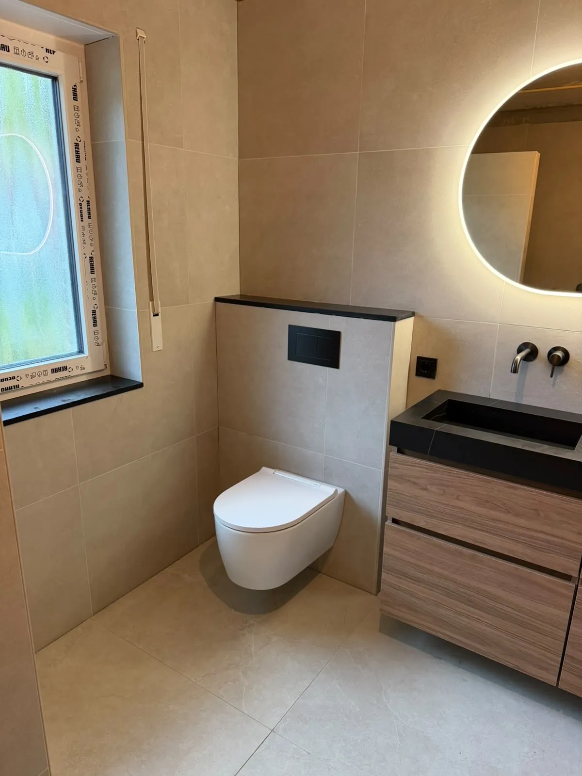 Badkamer met hangtoilet, houten badmeubel met zwart blad en ronde ledspiegel