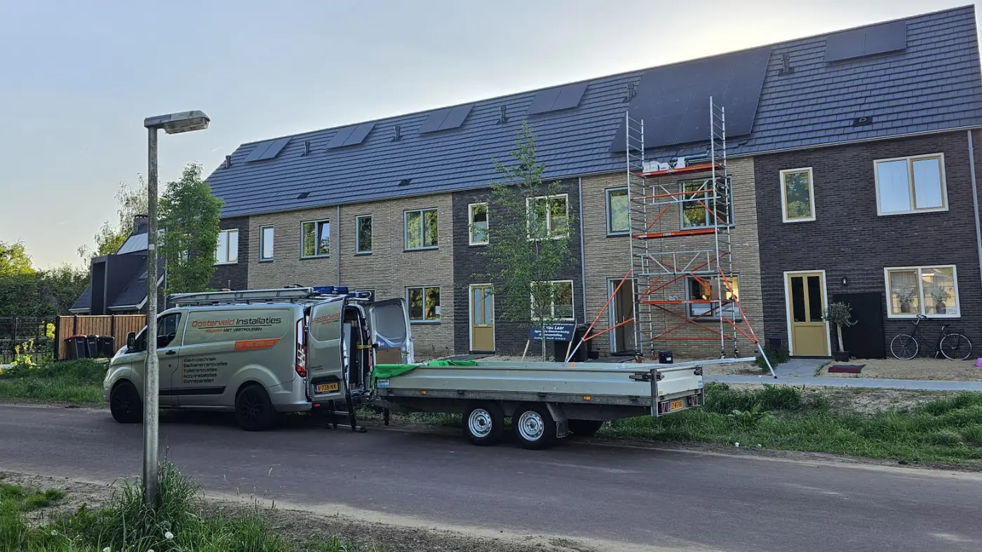 Bedrijfsbus met aanhanger bij een rij nieuwbouwwoningen met steigers