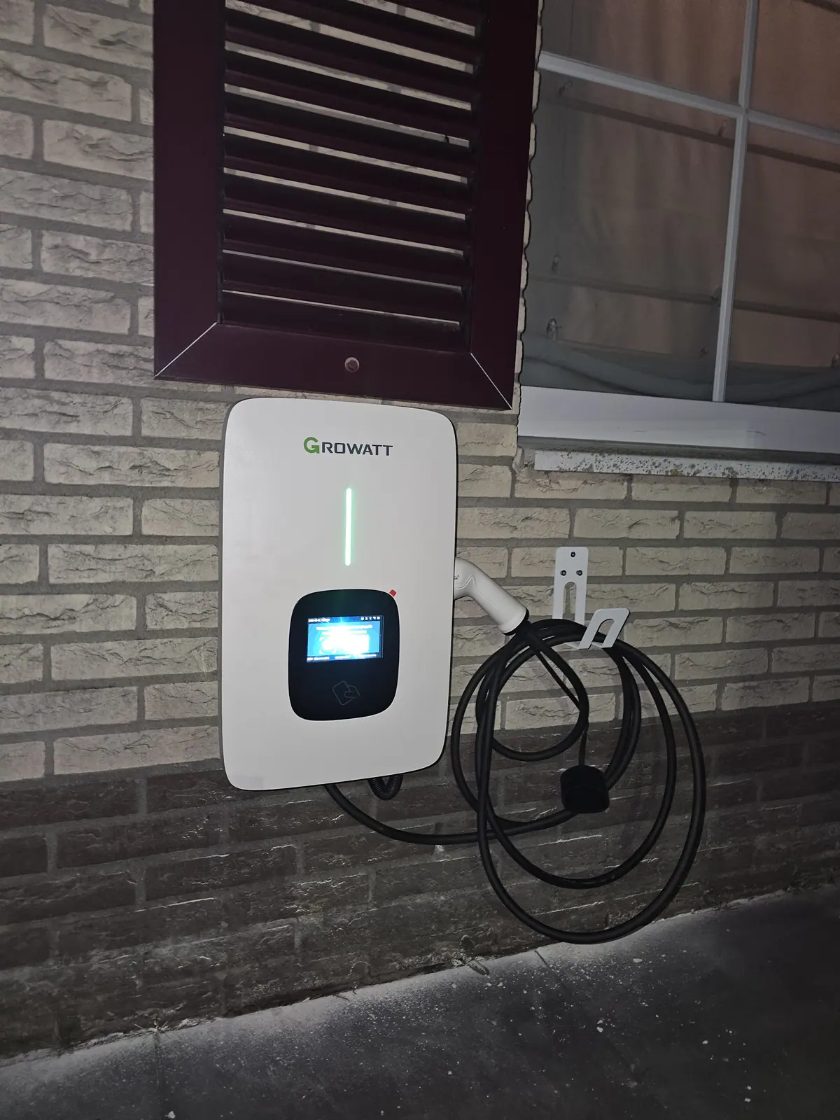 Laadpaal voor elektrische auto's aan een bakstenen gevel met opgerolde laadkabel