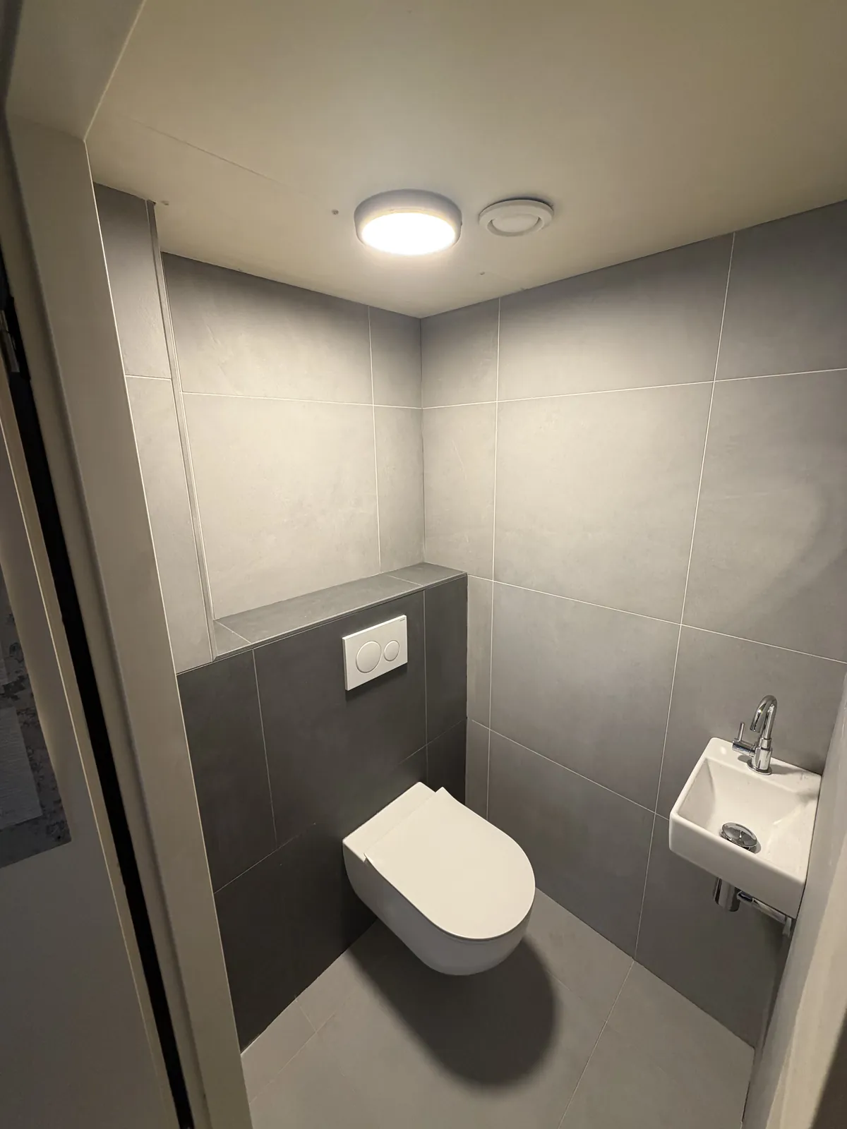 Toilet met donkere tegels, hangtoilet, inbouwreservoir en klein fonteintje