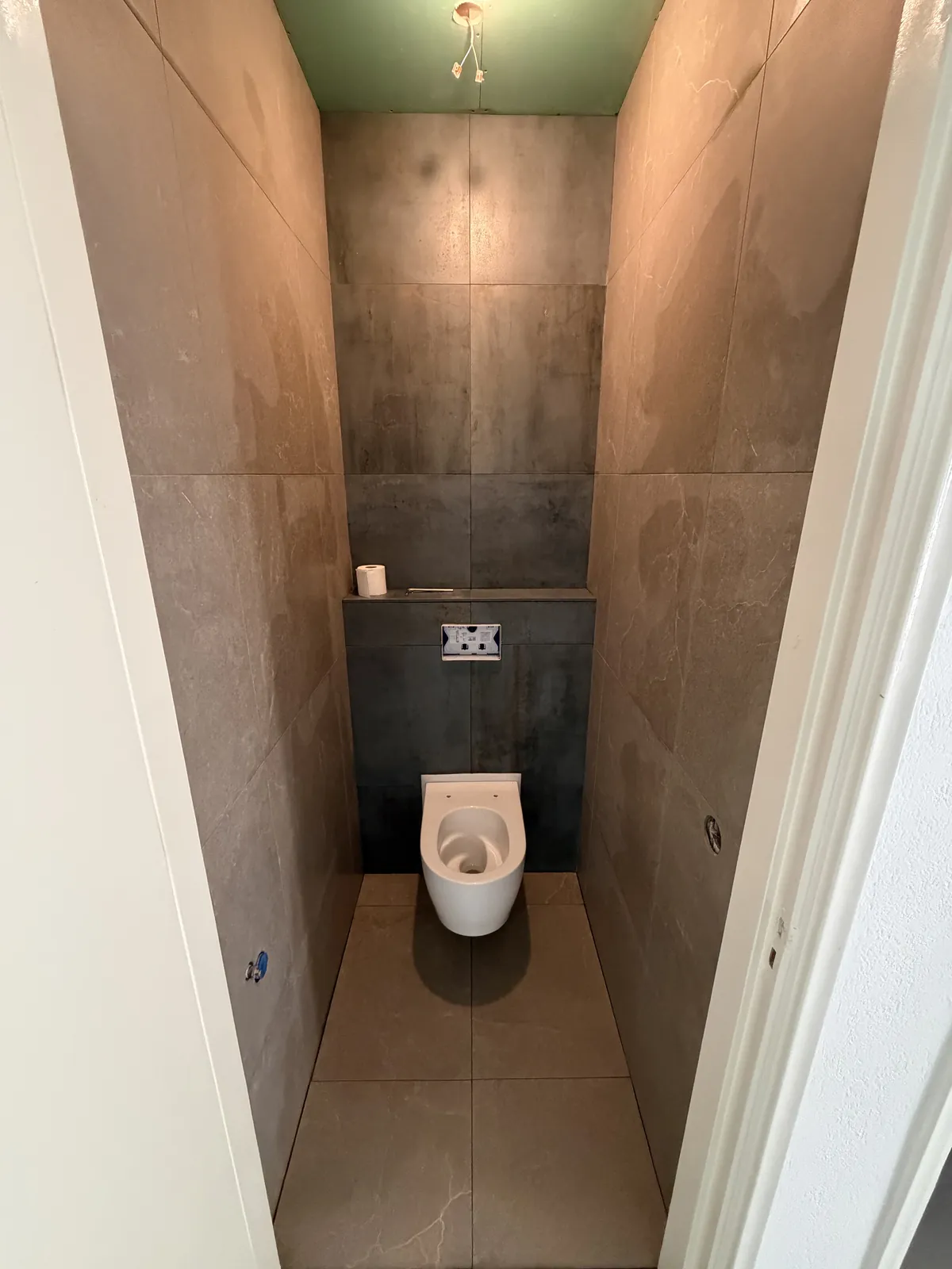Smal toilet met grote donkere tegels en een hangtoilet