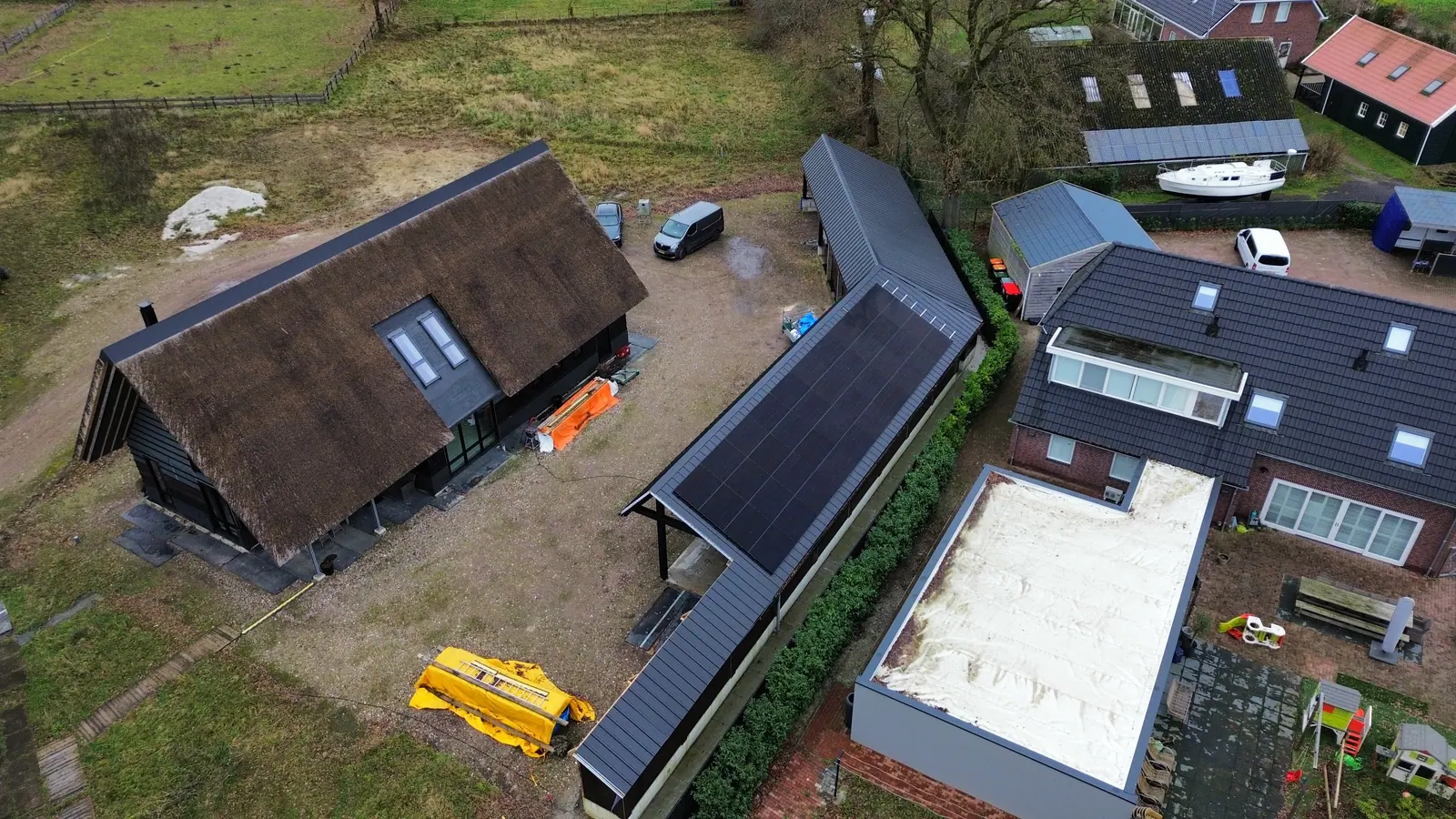 Rieten woning met bijgebouwen waarvan één dak zonnepanelen heeft, gezien vanuit de lucht